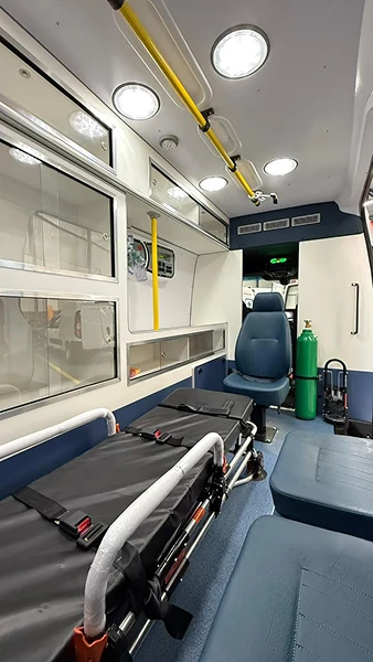 Interior de ambulância com maca preta, armários e poltrona azul