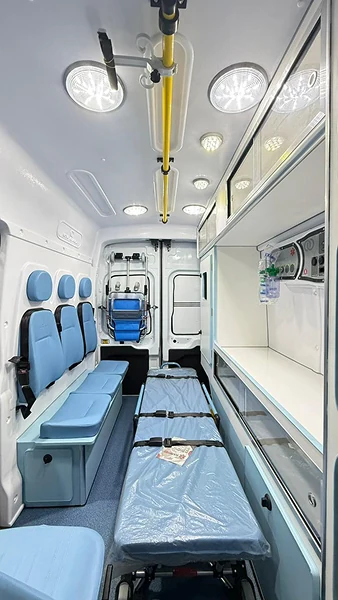Interior de ambulância com maca azul, bancos e armários brancos