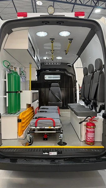 Interior de ambulância com maca, bancos cinza e cilindros verdes