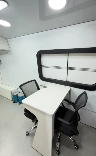 Sala de atendimento interna com mesa, cadeiras e janela lateral