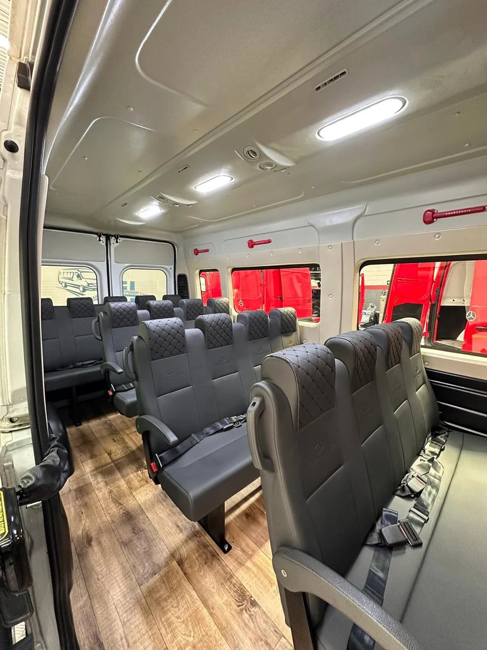 Interior de van com fileiras de bancos cinza e piso amadeirado