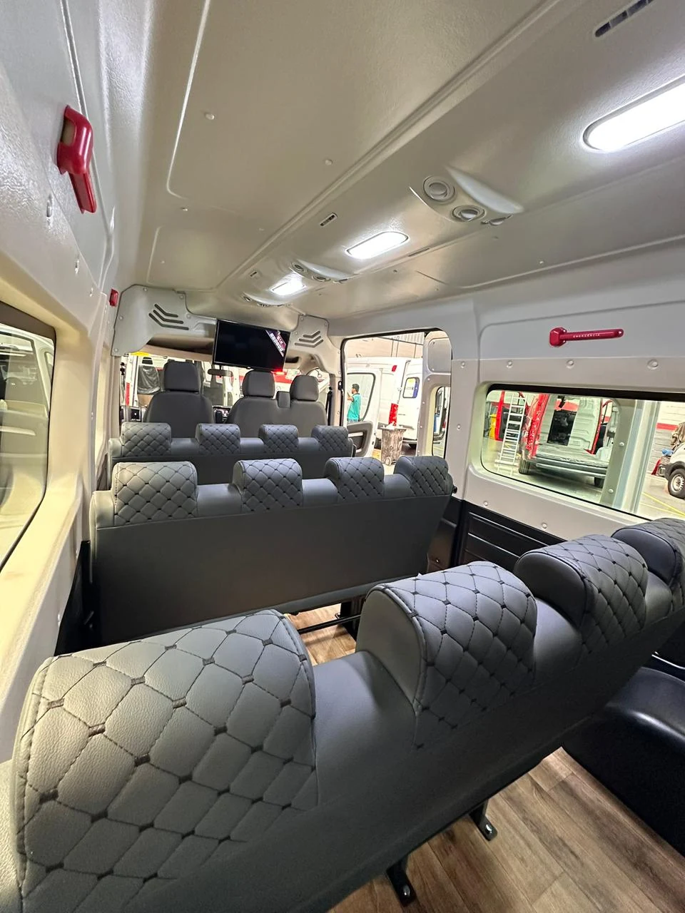 Cabine de passageiros com bancos cinza, iluminação no teto e monitor dianteiro